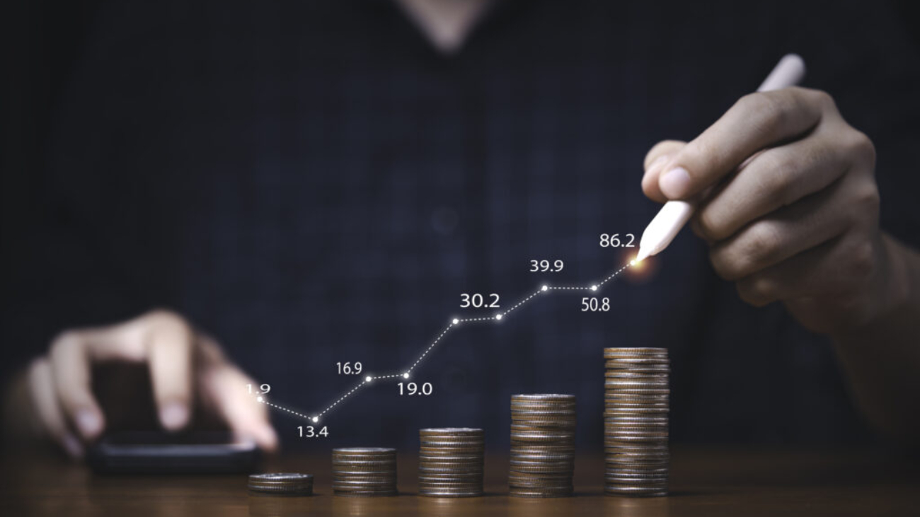 Trader writing increasing graph on coins stacking for investment profit growth and saving concept.