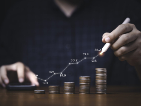 Trader writing increasing graph on coins stacking for investment profit growth and saving concept.